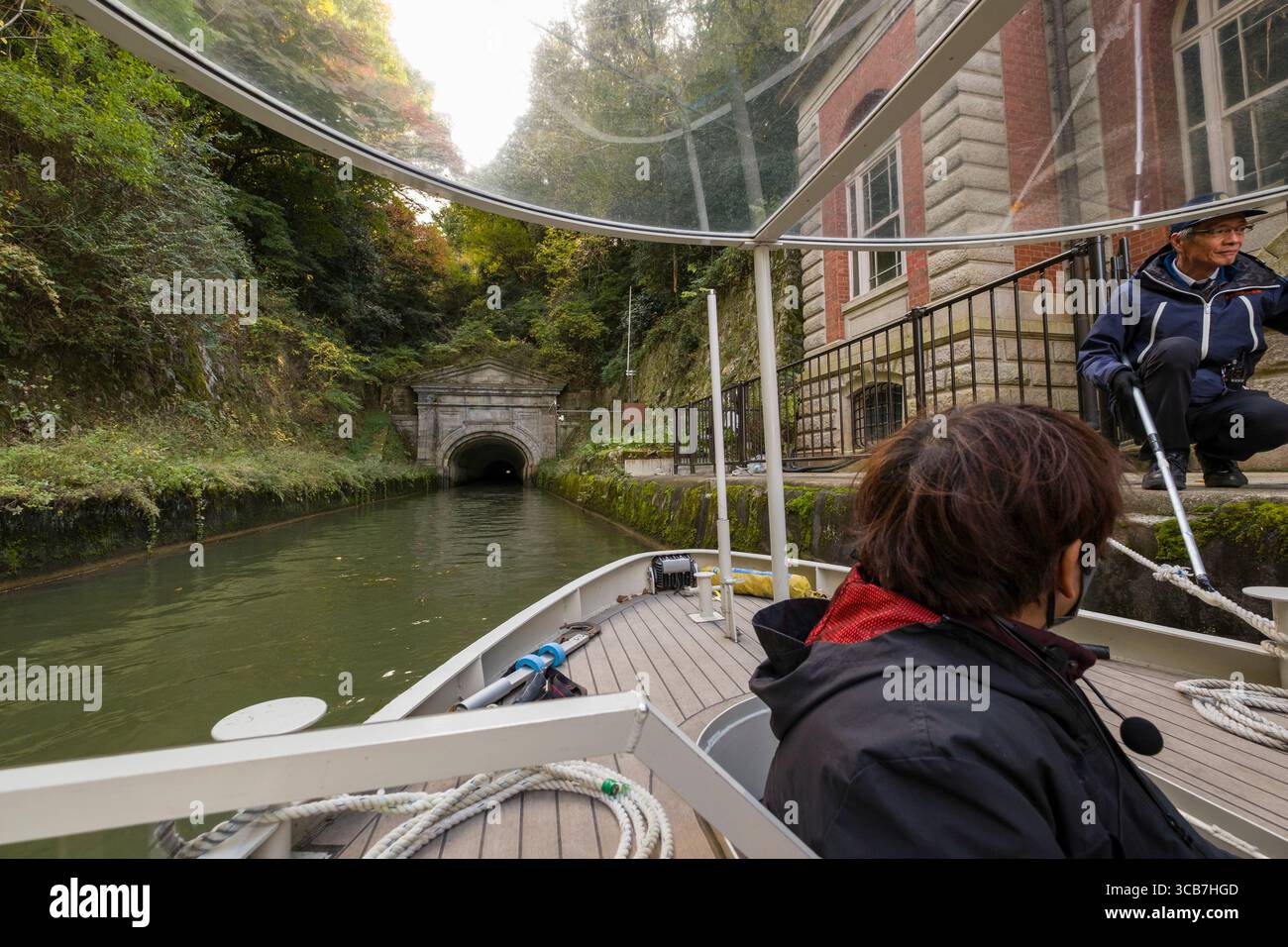 Die Bootstour auf dem See Biwa führt durch einen malerischen Kanaltunnel, umgeben von üppigem Grün und historischer Architektur, Kyoto, Japan Stockfoto