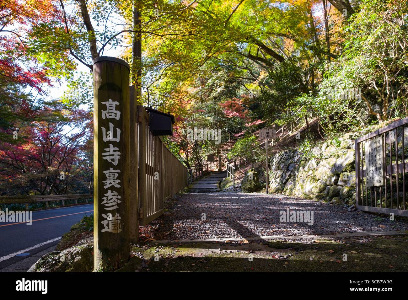 Pfad umgeben von lebhaftem Herbstlaub und Steinmauern, mit einem hölzernen Wegweiser mit japanischen Schriftzeichen, die ein ruhiges und Pictu schaffen Stockfoto