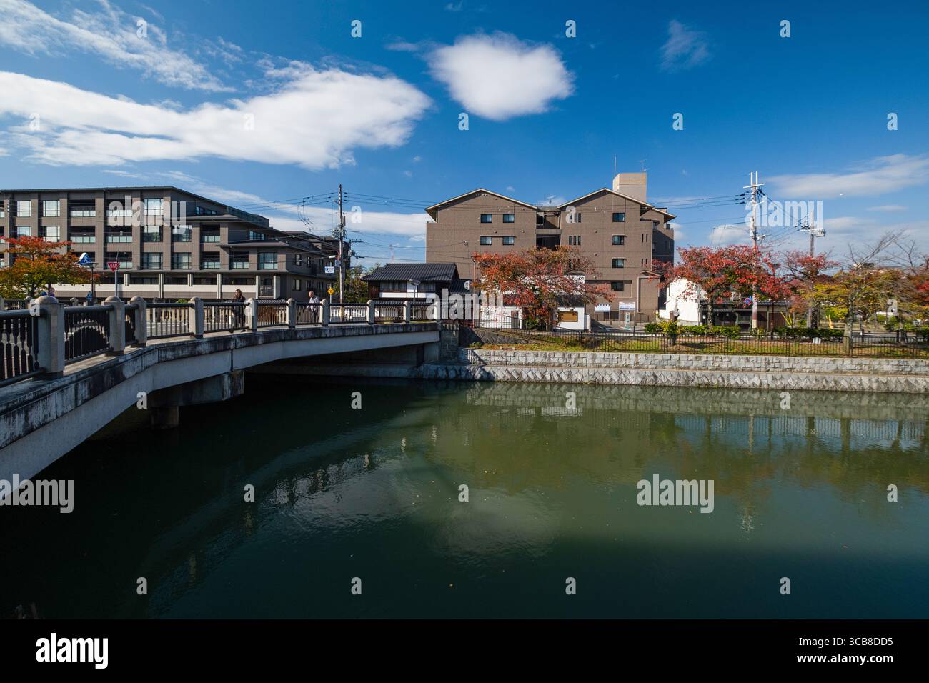 Lake Biwa Canal mit Reisen Bridge, Gebäuden und farbenfrohen Herbstbäumen unter einem sonnigen blauen Himmel. Reflexionen im Wasser verleihen diesem vibra Tiefe Stockfoto