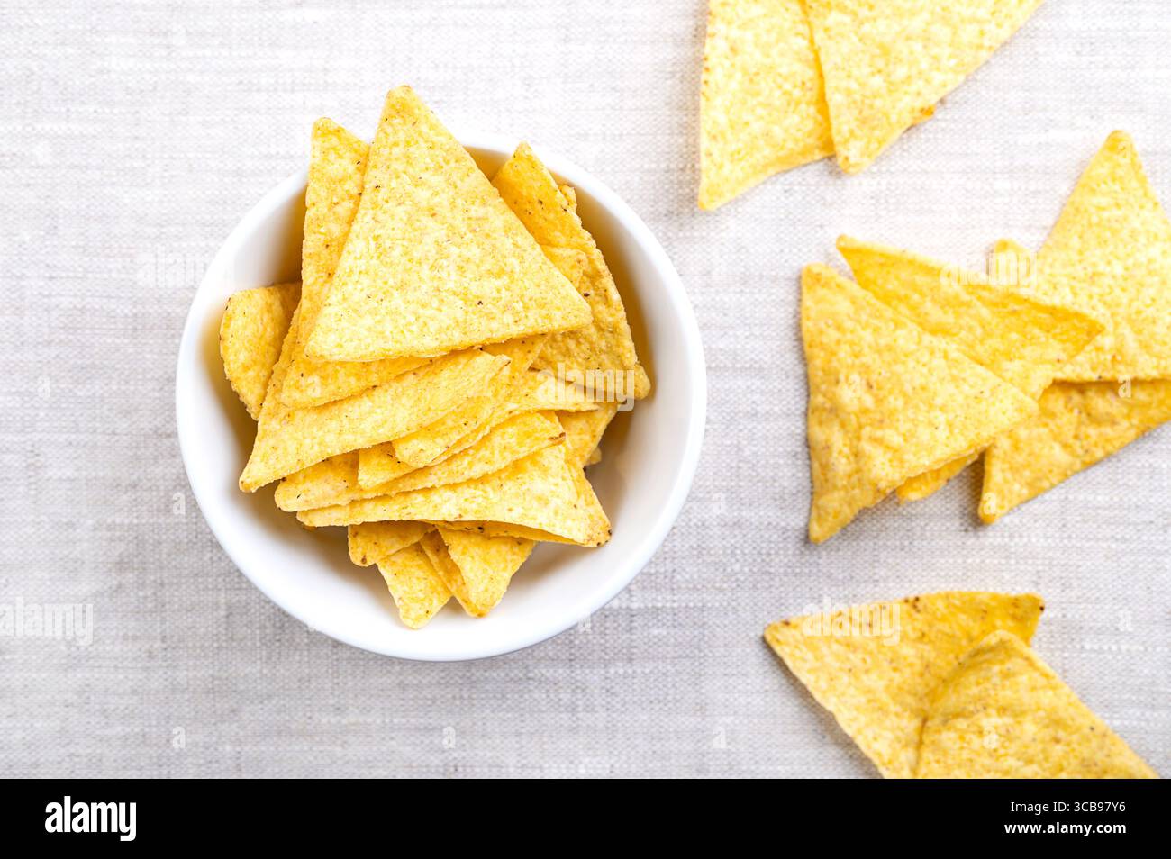 Tortillachips in weißer Schüssel auf Leinen. Klassische, knusprige Snacks aus Maistortillas, in dreieckige Keile geschnitten, in Öl frittiert und gesalzen Stockfoto