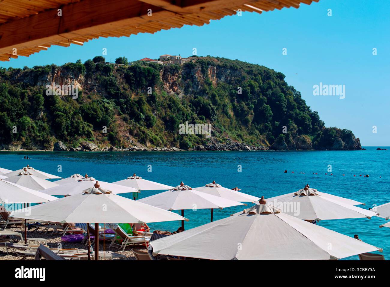 Ombrelloni contro il Mare e la costa rocciosa ad Himara in Albanien Stockfoto