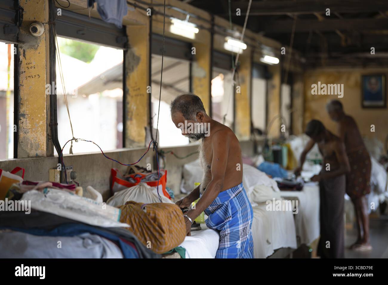 Mann, der mit traditionellem indischen Elektroeisen arbeitet, Dhobi Ghat, Freiluftwäsche in Kochi, Indien, altes Werkzeug zum Bügeln von Kleidung, 29.03.2025 Stockfoto