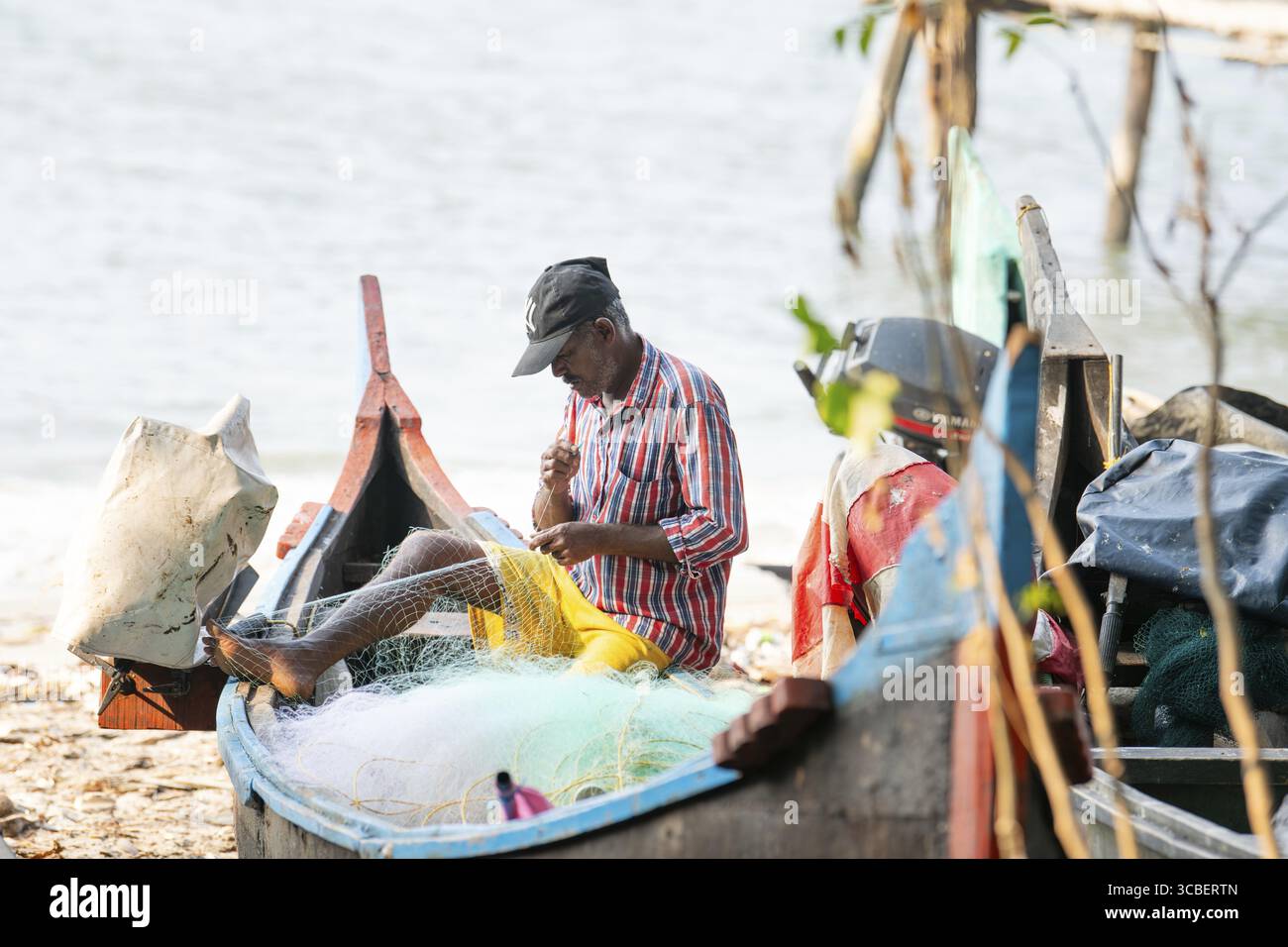 Fischer repariert traditionelles Fischernetz in seinem Boot, Strand von Kochi, Indien, Industrie an der arabischen Küste, 20.03.2025 Stockfoto