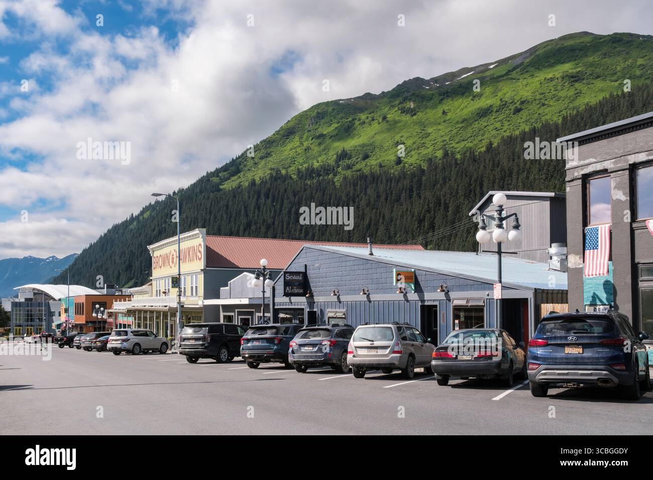 Autos parkten auf der Straße mit Geschäften in der alten alaskischen Südküste Stadt mit Blick auf das Sealife Centre. 3rd Avenue, Seward, Kenai Peninsula, Alaska, USA Stockfoto