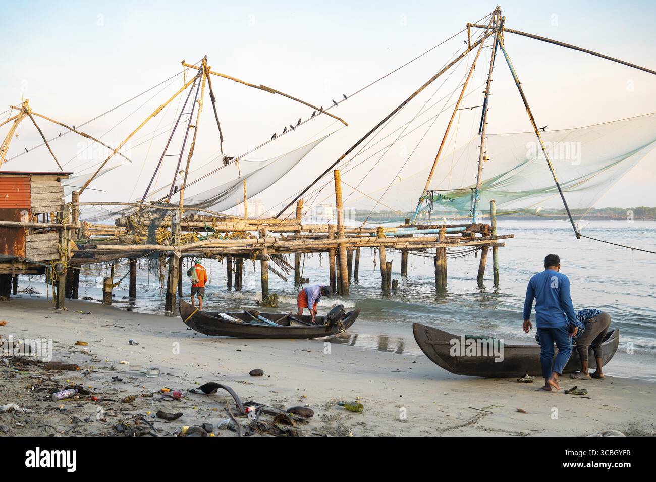 Fischer mit Boot neben chinesischen Fischernetzen am Ufer von Kochi, Kerala in Indien, Cheena vala oder Tangkul, traditionelles stationäres Liftnetz, 20,0 Stockfoto
