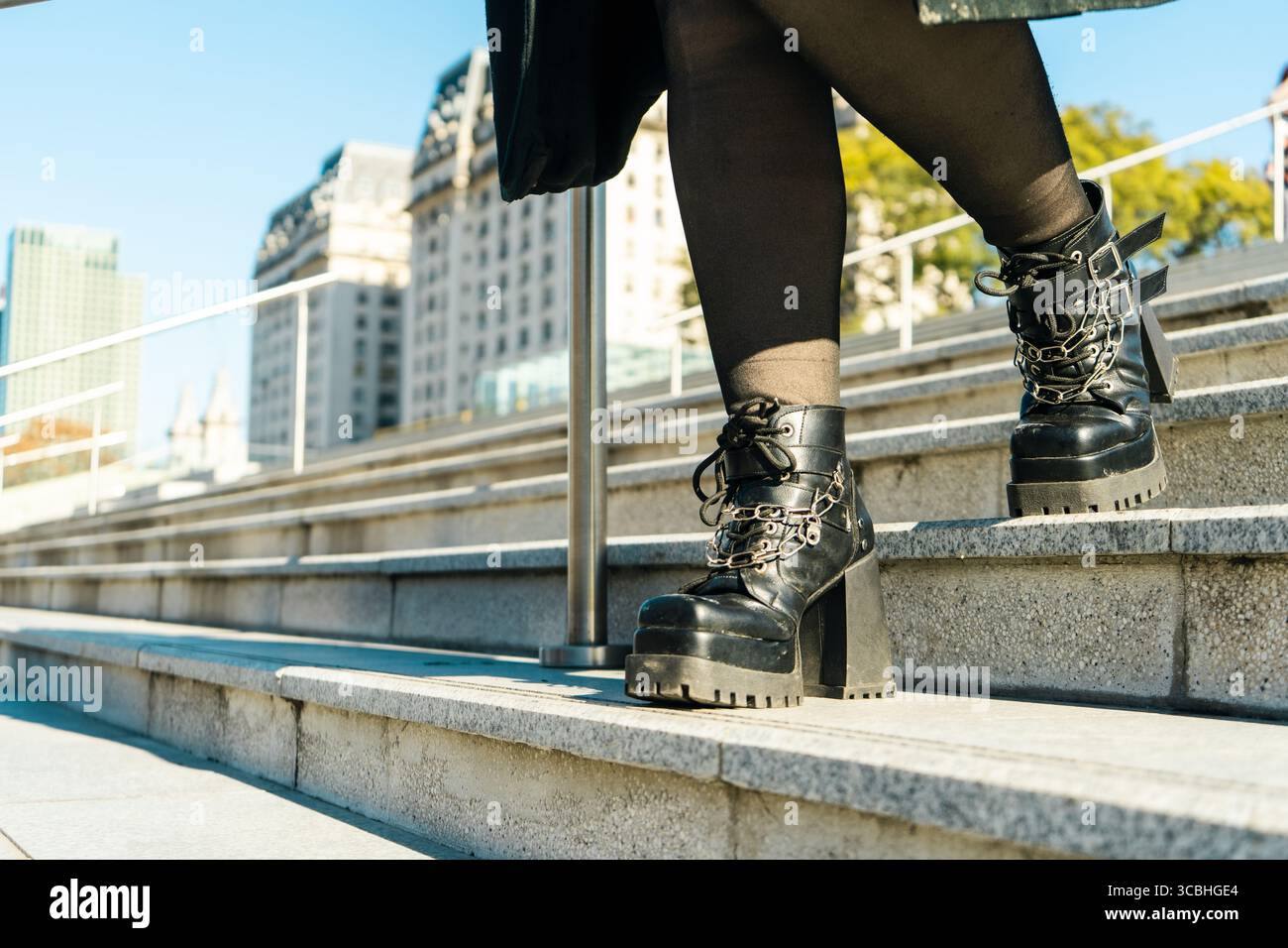 Nahaufnahme von Frauenbeinen, die in schwarzen Plateaustiefeln mit Ketten die Treppe hinuntergehen, mit urbaner Mode und Schuhen Stockfoto