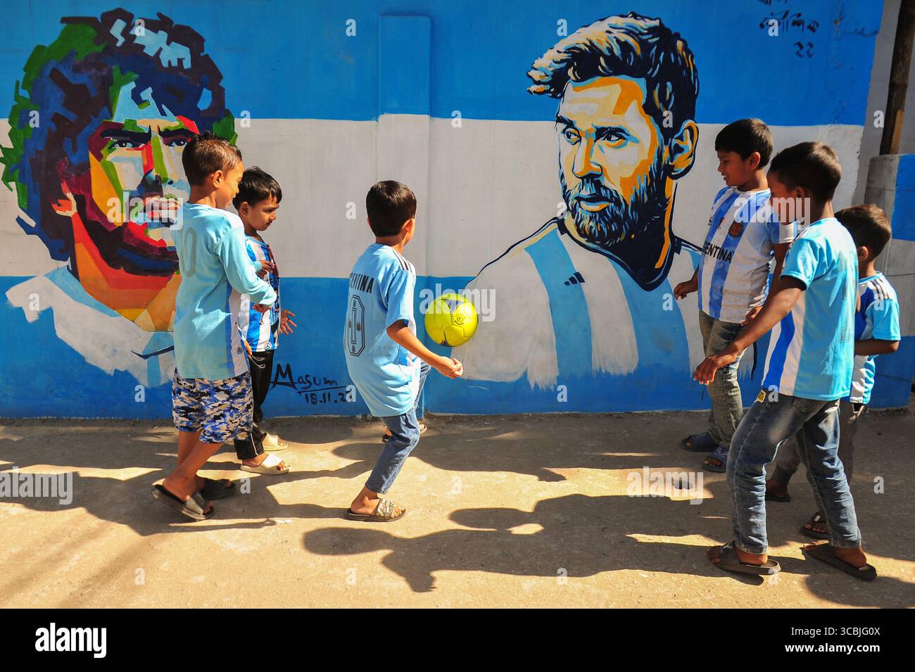 8. Dezember 2022, Sylhet, Bangladesch: 8. Dezember 2022 in Sylhet, Bangladesch: junge argentische Fans spielen Fußball auf der Straße von Sylhet, wo Graffiti von DIEGO MARADONA von der argentinischen Fußballmannschaft an der Wand gemalt ist. Bangladesch, ein solches Land, das nie für eine Fußball-Weltmeisterschaft qualifiziert wurde, aber große Liebe zum Fußball hat und riesige Fans sowohl für Argentinien als auch für Brasilien hat. (Bild: © MD Rafayat Haque Khan/ZUMA Press Wire) Stockfoto