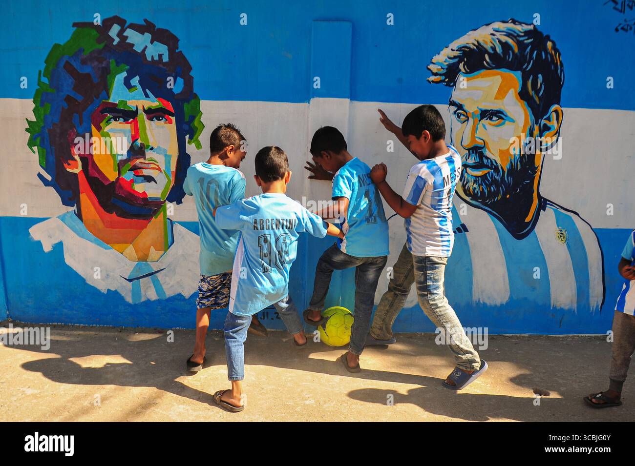 8. Dezember 2022, Sylhet, Bangladesch: 8. Dezember 2022 in Sylhet, Bangladesch: junge argentische Fans spielen Fußball auf der Straße von Sylhet, wo Graffiti von DIEGO MARADONA von der argentinischen Fußballmannschaft an der Wand gemalt ist. Bangladesch, ein solches Land, das nie für eine Fußball-Weltmeisterschaft qualifiziert wurde, aber große Liebe zum Fußball hat und riesige Fans sowohl für Argentinien als auch für Brasilien hat. (Bild: © MD Rafayat Haque Khan/ZUMA Press Wire) Stockfoto