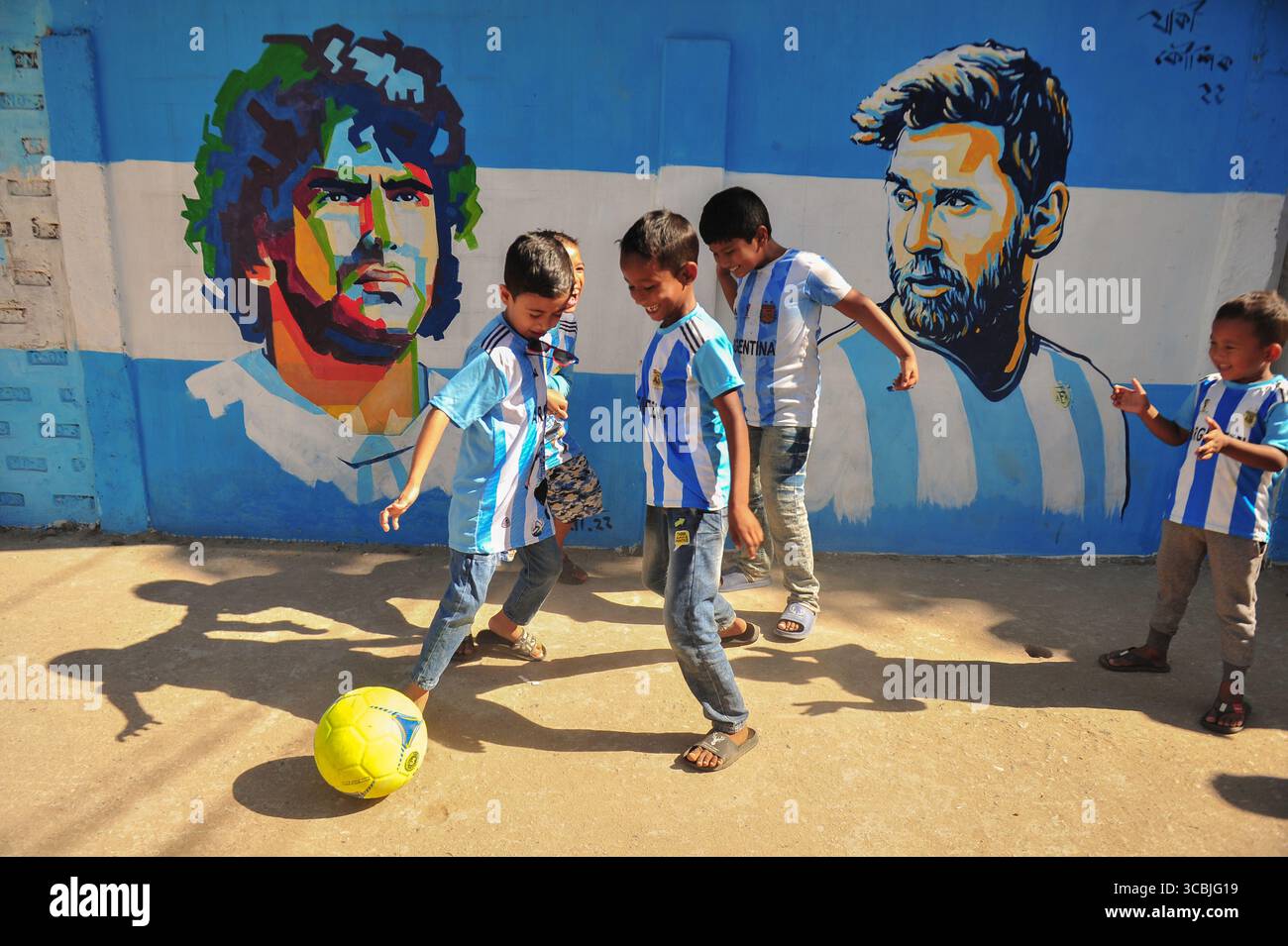 8. Dezember 2022, Sylhet, Bangladesch: 8. Dezember 2022 in Sylhet, Bangladesch: junge argentische Fans spielen Fußball auf der Straße von Sylhet, wo Graffiti von DIEGO MARADONA von der argentinischen Fußballmannschaft an der Wand gemalt ist. Bangladesch, ein solches Land, das nie für eine Fußball-Weltmeisterschaft qualifiziert wurde, aber große Liebe zum Fußball hat und riesige Fans sowohl für Argentinien als auch für Brasilien hat. (Bild: © MD Rafayat Haque Khan/ZUMA Press Wire) Stockfoto