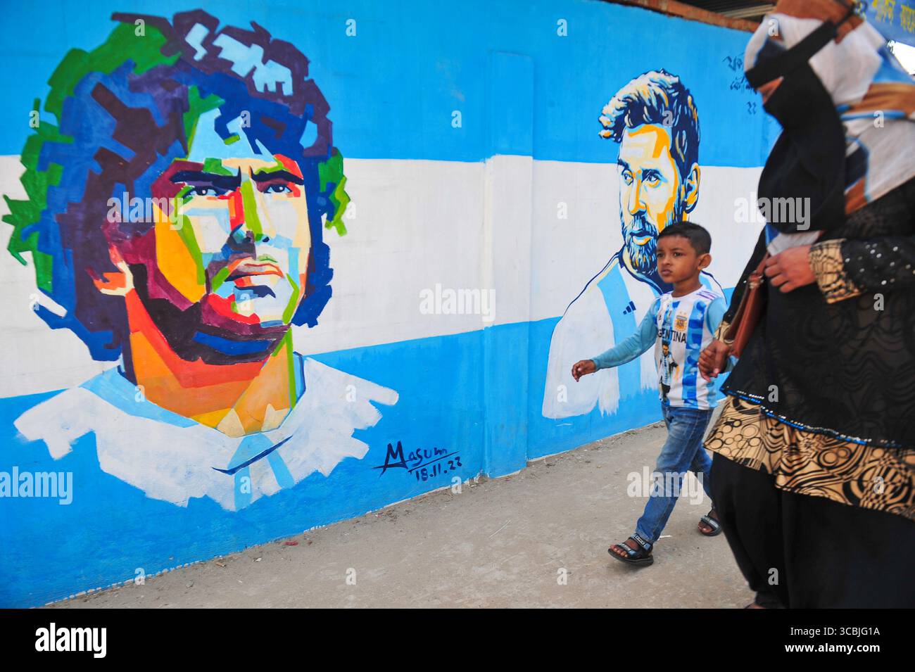 8. Dezember 2022: 8. Dezember 2022: Sylhet, Bangladesch: Junge argentische Fans gehen mit seiner Mutter auf die Straße von Sylhet, wo Graffiti von DIEGO MARADONA von der argentinischen Fußballmannschaft an die Wand gemalt ist. Bangladesch, ein solches Land, das nie für eine Fußball-Weltmeisterschaft qualifiziert wurde, aber große Liebe zum Fußball hat und riesige Fans sowohl für Argentinien als auch für Brasilien hat. (Bild: © MD Rafayat Haque Khan/ZUMA Press Wire) Stockfoto
