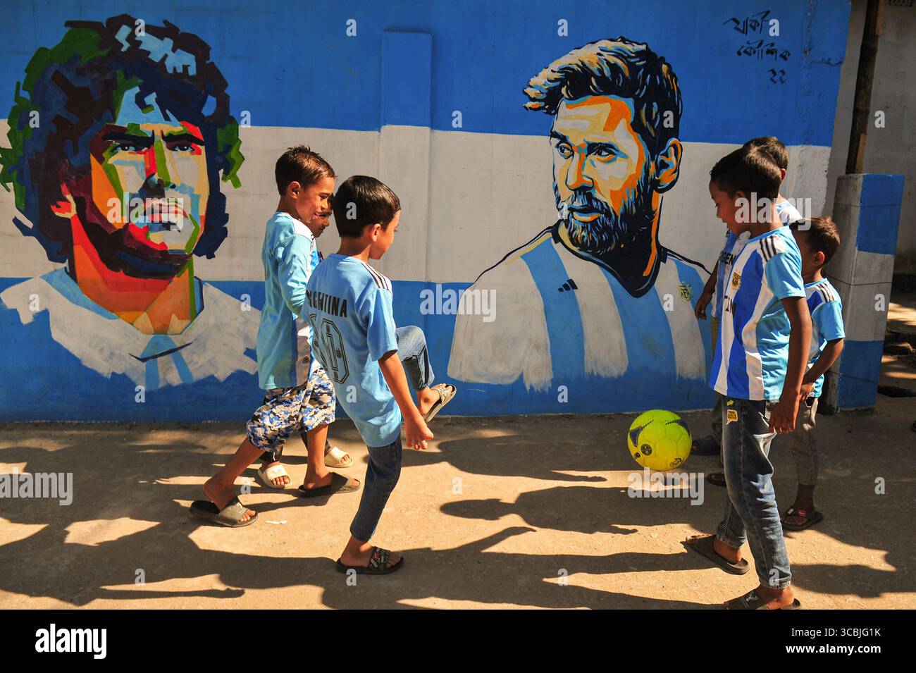 8. Dezember 2022, Sylhet, Bangladesch: 8. Dezember 2022 in Sylhet, Bangladesch: junge argentische Fans spielen Fußball auf der Straße von Sylhet, wo Graffiti von DIEGO MARADONA von der argentinischen Fußballmannschaft an der Wand gemalt ist. Bangladesch, ein solches Land, das nie für eine Fußball-Weltmeisterschaft qualifiziert wurde, aber große Liebe zum Fußball hat und riesige Fans sowohl für Argentinien als auch für Brasilien hat. (Bild: © MD Rafayat Haque Khan/ZUMA Press Wire) Stockfoto