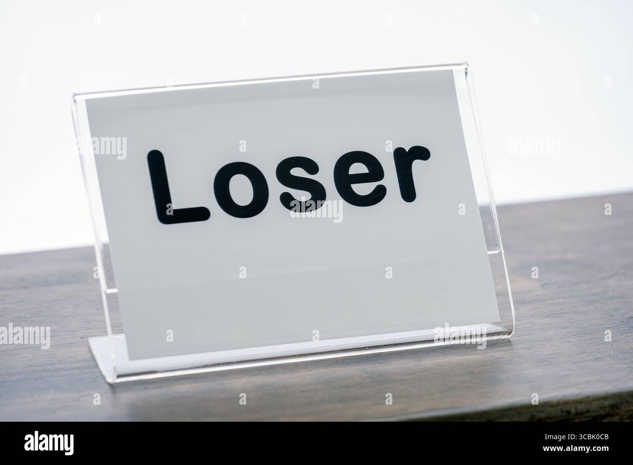 Ein Schild mit dem Wort Loser steht auf dem Holztheke, das humorvolle oder sarkastische Botschaften vermittelt. Das Schild ist mit einem transparenten Kunststoffhalter ummantelt, wodurch hervorgehoben wird Stockfoto