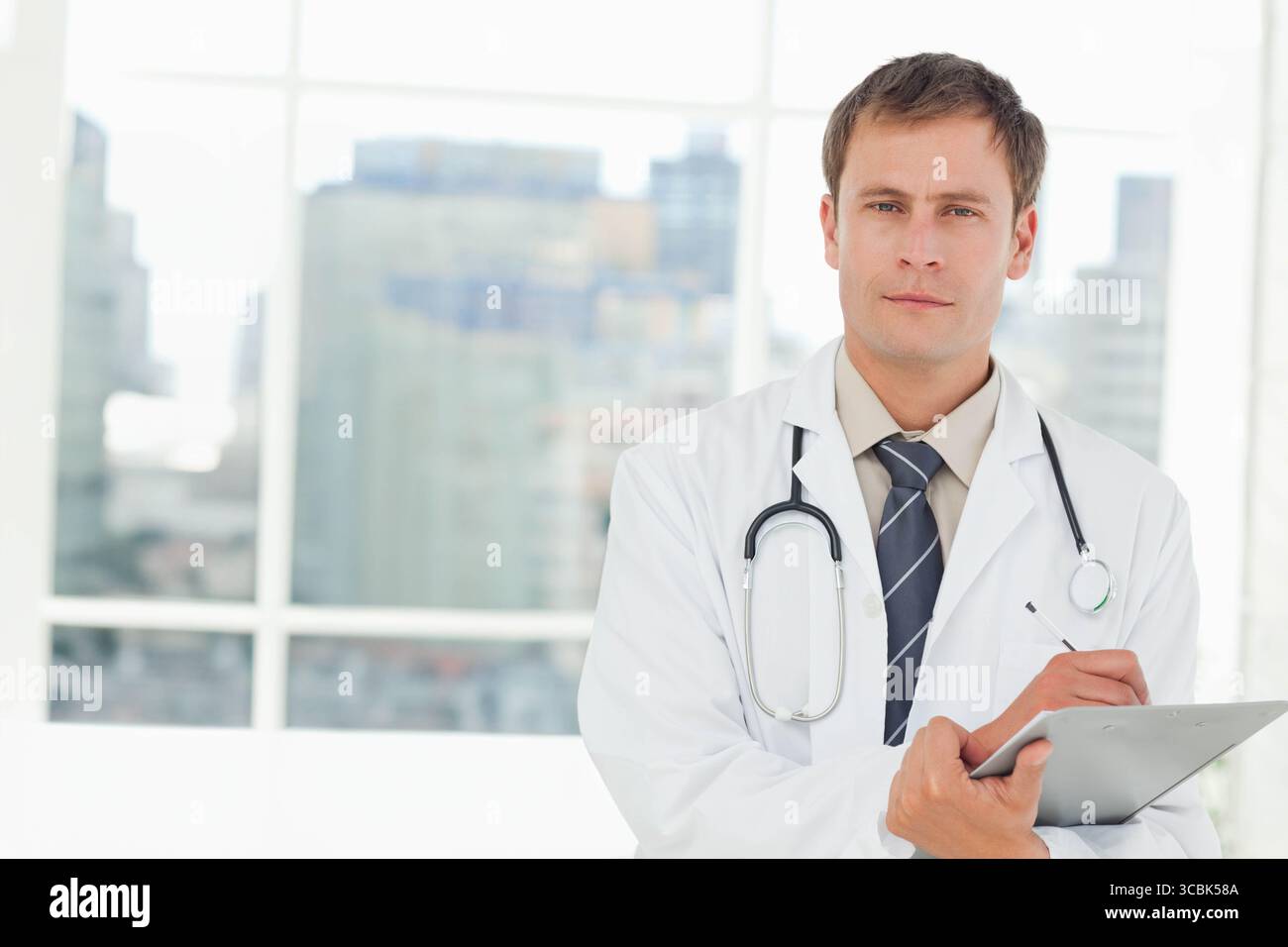 Männlicher Arzt, der im Büro Schreibstift auf der Zwischenablage hält, mit weißem Mantel, Stethoskop, Kopierraum. Medizin, Professionalität, Gesundheitswesen, Urban, Clini Stockfoto