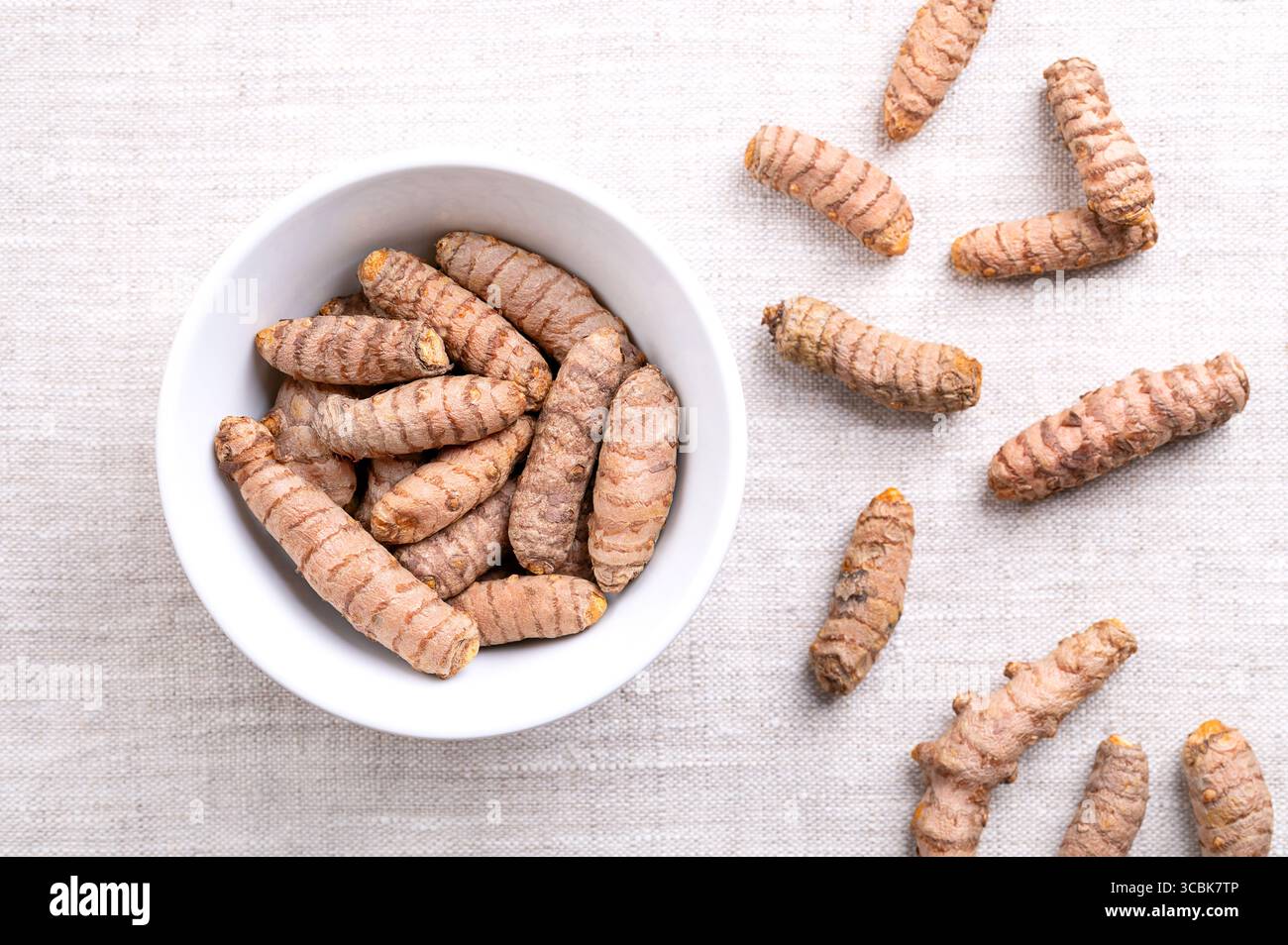 Frische Kurkuma-Rhizome, in einer weißen Schüssel, auf Leinen. Unterirdische Stämme der Kurkuma-Pflanze Curcuma longa, mit hellem Orangenfleisch. Stockfoto