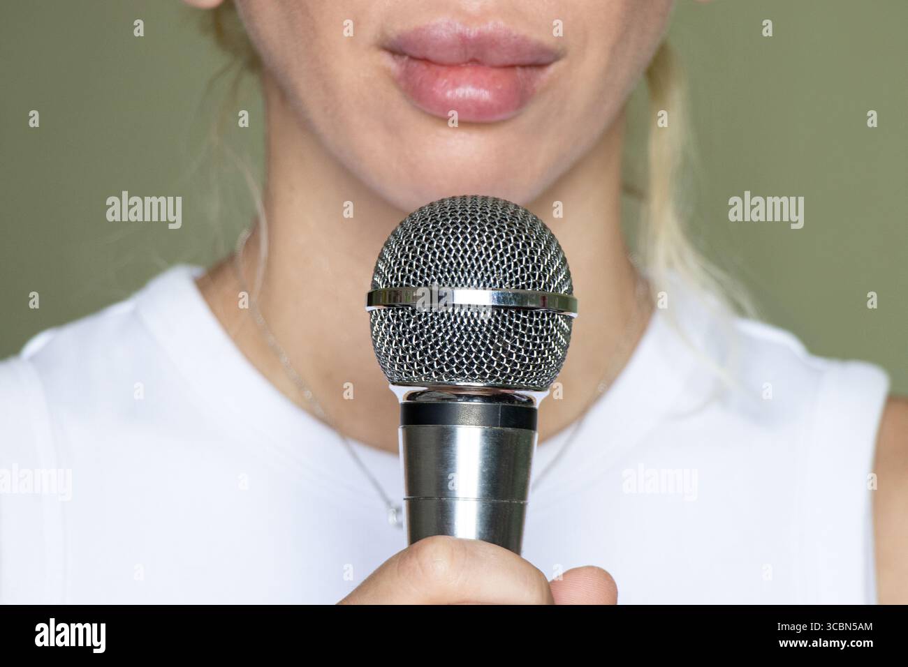 Frau mit Mikrofon vor dem Mund, Nahaufnahme von Gesicht und Hand, Vorbereitung auf das Singen oder Aufführen auf grünem Hintergrund zu Hause Stockfoto