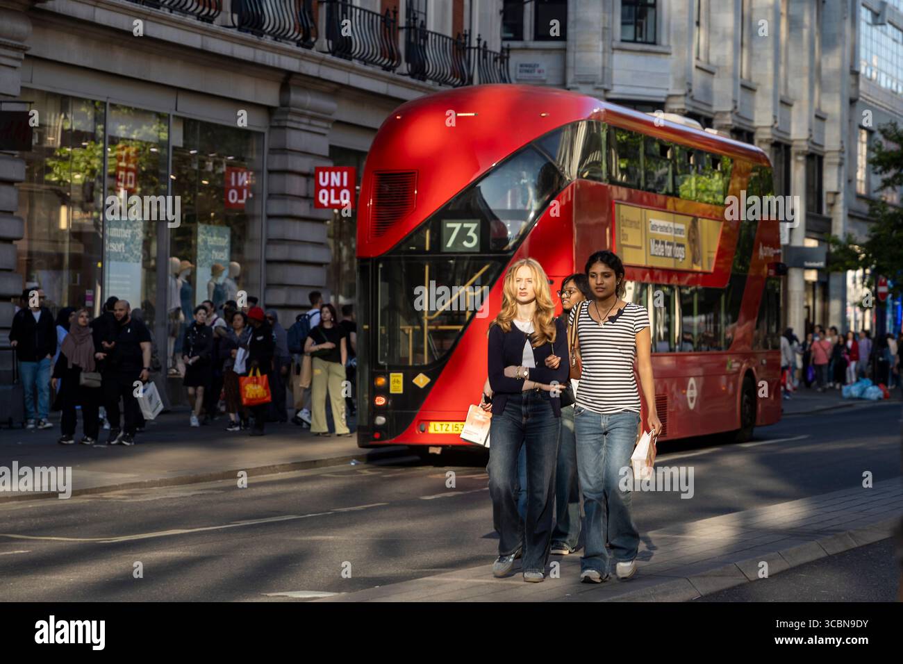 London, UK, 5. Mai 2025, zwei junge Frauen, eine blonde und eine mit dunklem Haar, gehen im Vordergrund, lässig in Jeans und Oberteilen gekleidet, trage einen Laden Stockfoto
