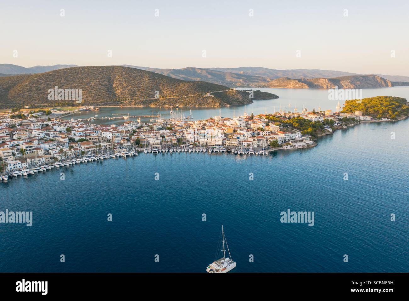 Blick aus der Vogelperspektive auf eine griechische Stadt, eingebettet am azurblauen Meer, einem Wandteppich aus sonnengeküssten Dächern und verwinkelten Gassen, mit fernen Bergen, Ermioni, Argolis, Griechenland. Stockfoto