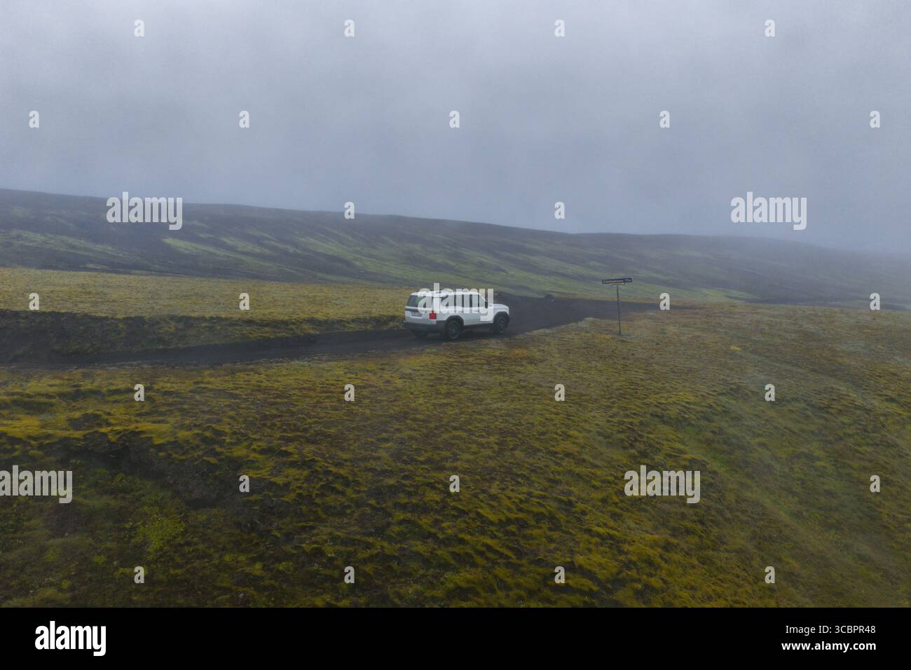 Weißer SUV auf einer Schotterstraße in Islands moosbedecktem vulkanischem Gelände Stockfoto
