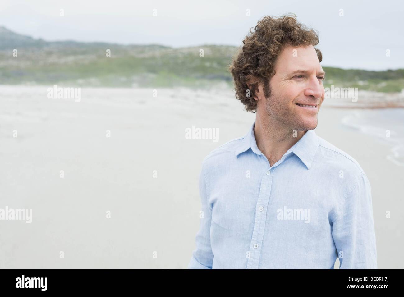 Mann, der am Sandstrand steht, trägt ein hellblaues Leinenhemd und sieht rechts aus, Kopierraum Stockfoto