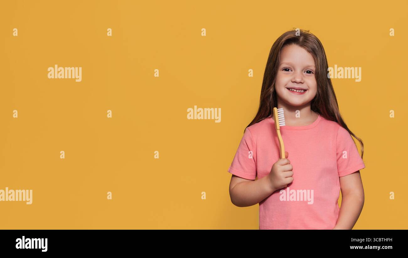 Ein glückliches Mädchen hält eine Zahnbürste in den Händen. Eine isolierte Panoramaaufnahme. Ein Ort für Ihre SMS. Kinderzahnheilkunde Stockfoto
