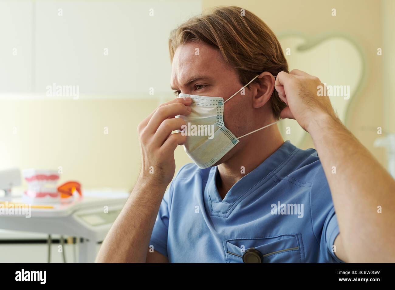 Kaukasischer junger erwachsener Mann, der medizinische Peelings trägt, die chirurgische Maske auf dem Gesicht in der klinischen Umgebung, Vorbereitung für das Gesundheitswesen Eingriff, fokussierter Ausdruck sichtbar Stockfoto