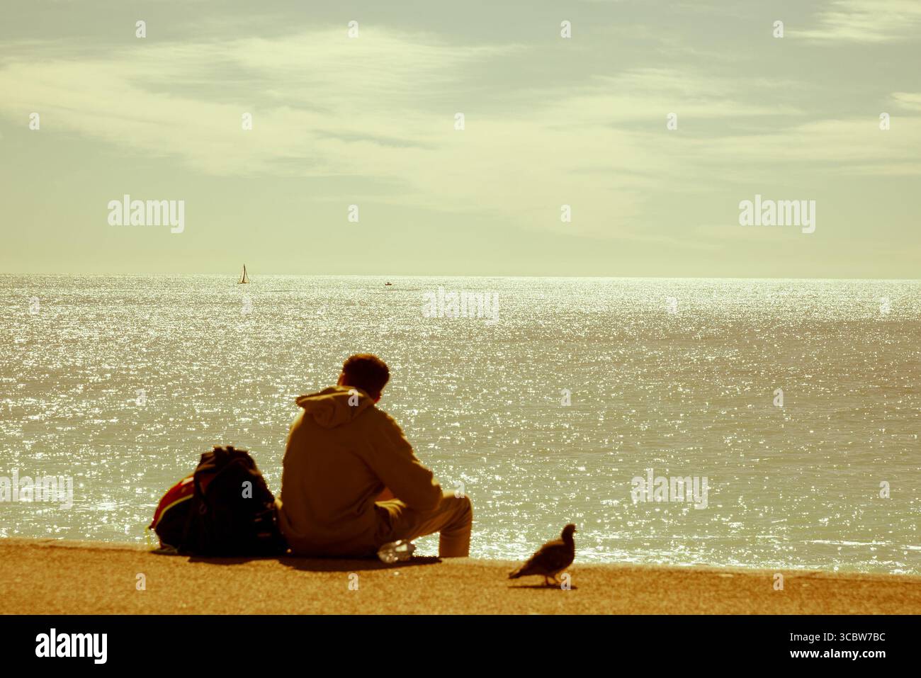 Unfokussierte Person, die am Strand sitzt und in die Ferne blickt Stockfoto