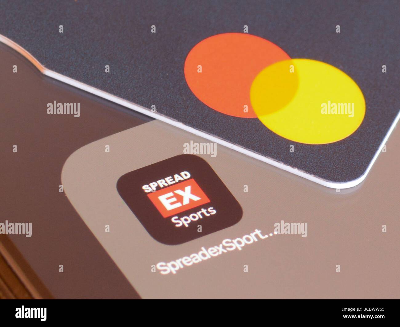 SpreadexSports tauscht Glücksspiel-App auf dem Smartphone-Bildschirm mit Mastercard Debitkarte um Geld einzuzahlen Stockfoto