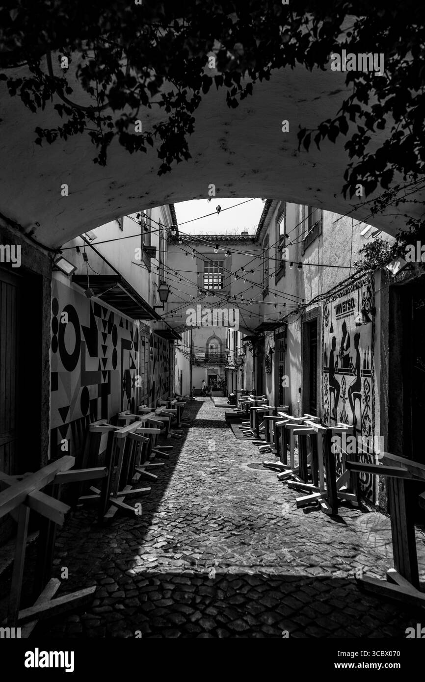 Algarve, Portugal – 2025.06.28 Eine verzierte Gasse mit Wandmalereien und Lichterketten über leeren Cafés in der historischen Stadt Stockfoto