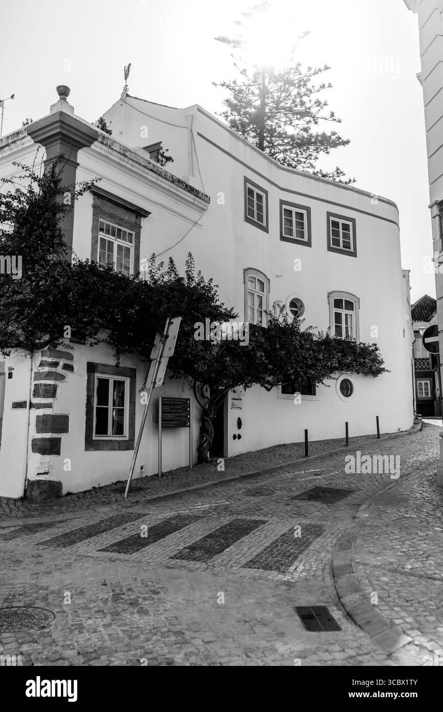 Tavira, Algarve, Portugal – 2025.07.02: Sonniger Eckblick auf weiß getünchte historische Gebäude mit Bougainvillea, Kopfsteinpflasterstraßen und trad Stockfoto