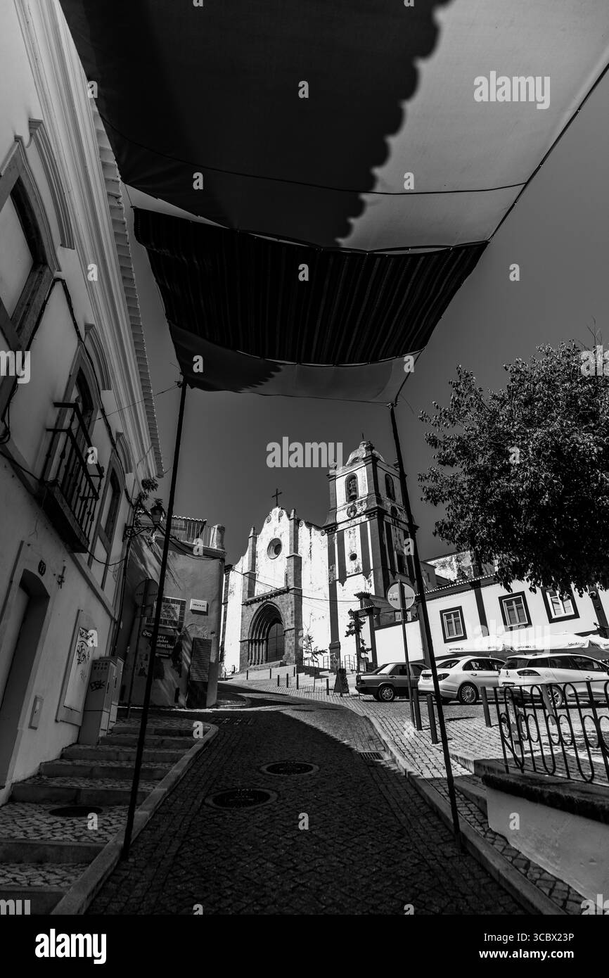 Silves, Algarve, Portugal – 2025.07.04: Straßenblick auf die historische Silves Kathedrale mit ihrem gotischen Eingang, eingerahmt von gestreiften Stoffdächern Stockfoto