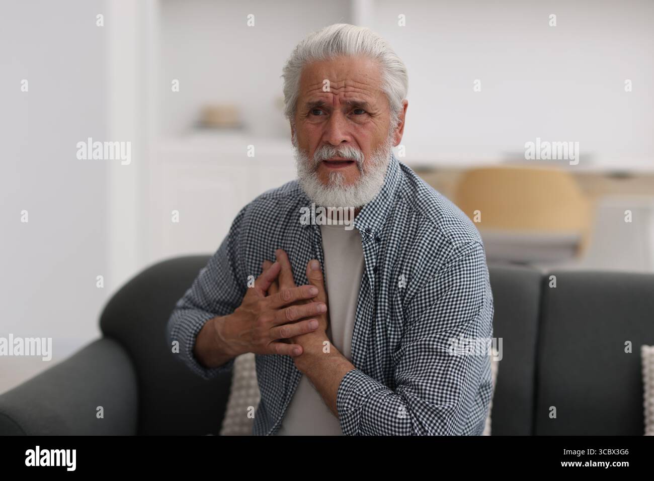 Ein älterer Mann, der zu Hause an Brustschmerzen leidet Stockfoto