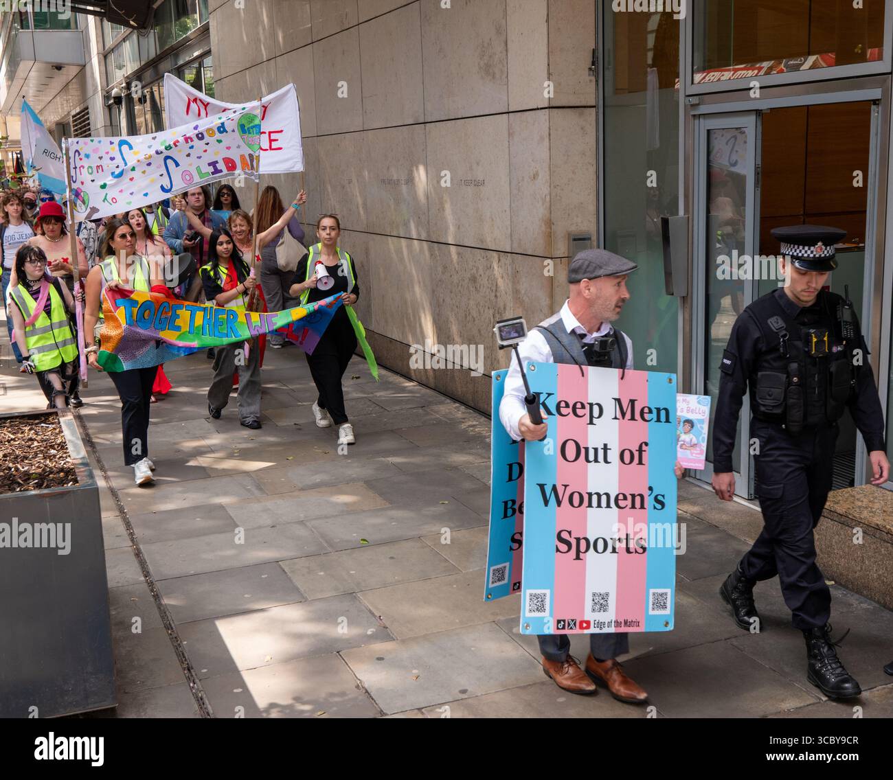 Der Anti-Trans-Streamer läuft mit einem Polizisten vor dem britischen frauenmarsch Manchester mit einem Schild zum Halten der Männer aus dem Frauensport. Demonstranten marschierten durch das Zentrum von manchester. Schilder zeigten, dass Frauen häusliche Gewalt vergewaltigen. Anti-Trans, ihr Röhren-Streamer und Demonstranten flankiert den Protest. Manchester UK. Bild: Garyrobertsphotographie Stockfoto
