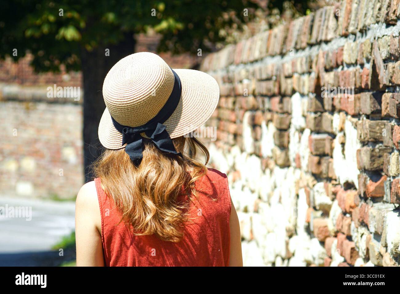 Rückansicht einer Frau in Sommerkleid und Hut, die neben der Backsteinmauer der Kalemegdan Festung spaziert. Konzept des langsamen Tourismus und des europäischen Erbes Stockfoto