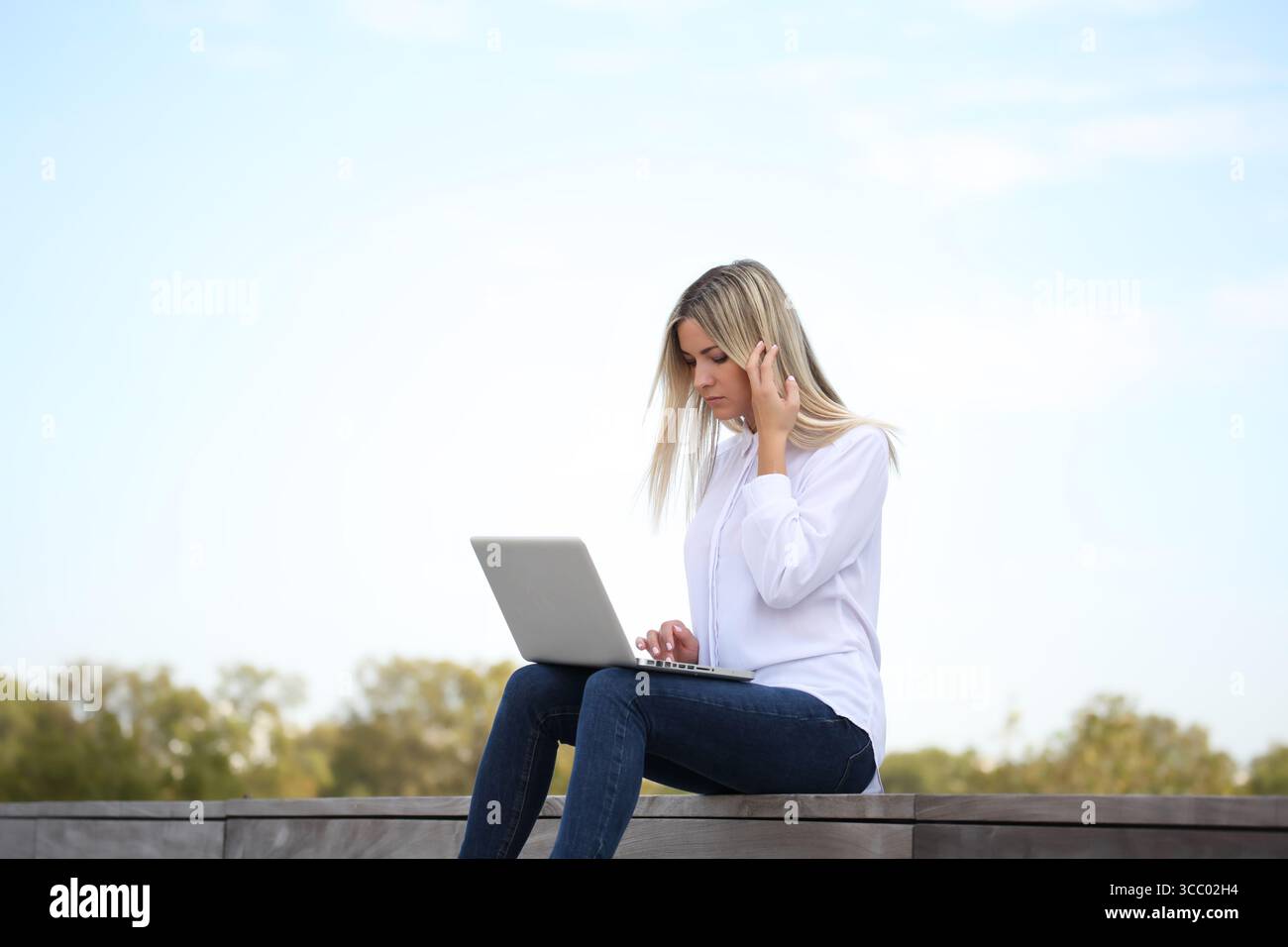 JUNGE BLONDE FRAU, DIE DRAUSSEN AUF IHREM LAPTOP ARBEITET Stockfoto JUNGE BLONDE FRAU, DIE DRAUSSEN AUF IHREM LAPTOP ARBEITET Stockfoto