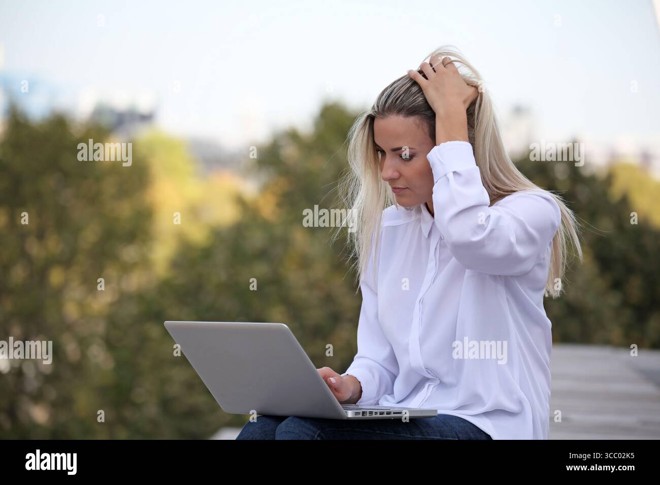 JUNGE BLONDE FRAU, DIE DRAUSSEN AUF IHREM LAPTOP ARBEITET Stockfoto JUNGE BLONDE FRAU, DIE DRAUSSEN AUF IHREM LAPTOP ARBEITET Stockfoto