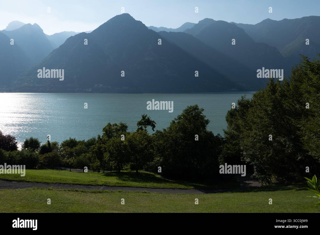 Die sonnige Wiese überblickt den Idro-See in Brescia, Italien, mit alpinen Bergen und ruhigem blauem Wasser, die eine ruhige Sommerszene schaffen. Stockfoto