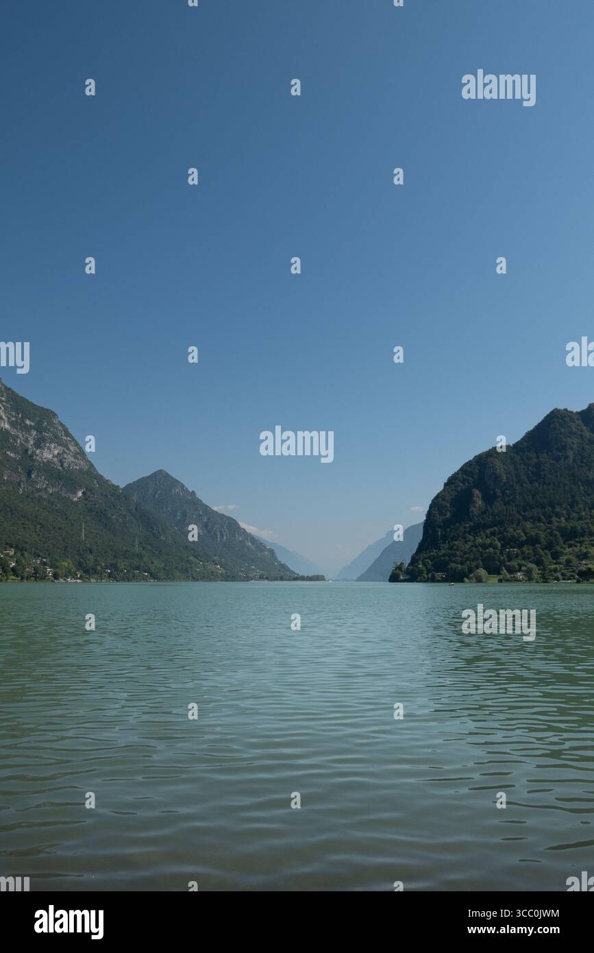 Das türkisfarbene Wasser des Idro-Sees in Brescia, Italien, schimmert unter einem klaren Sommerhimmel, umgeben von friedlichen Bergen. Stockfoto