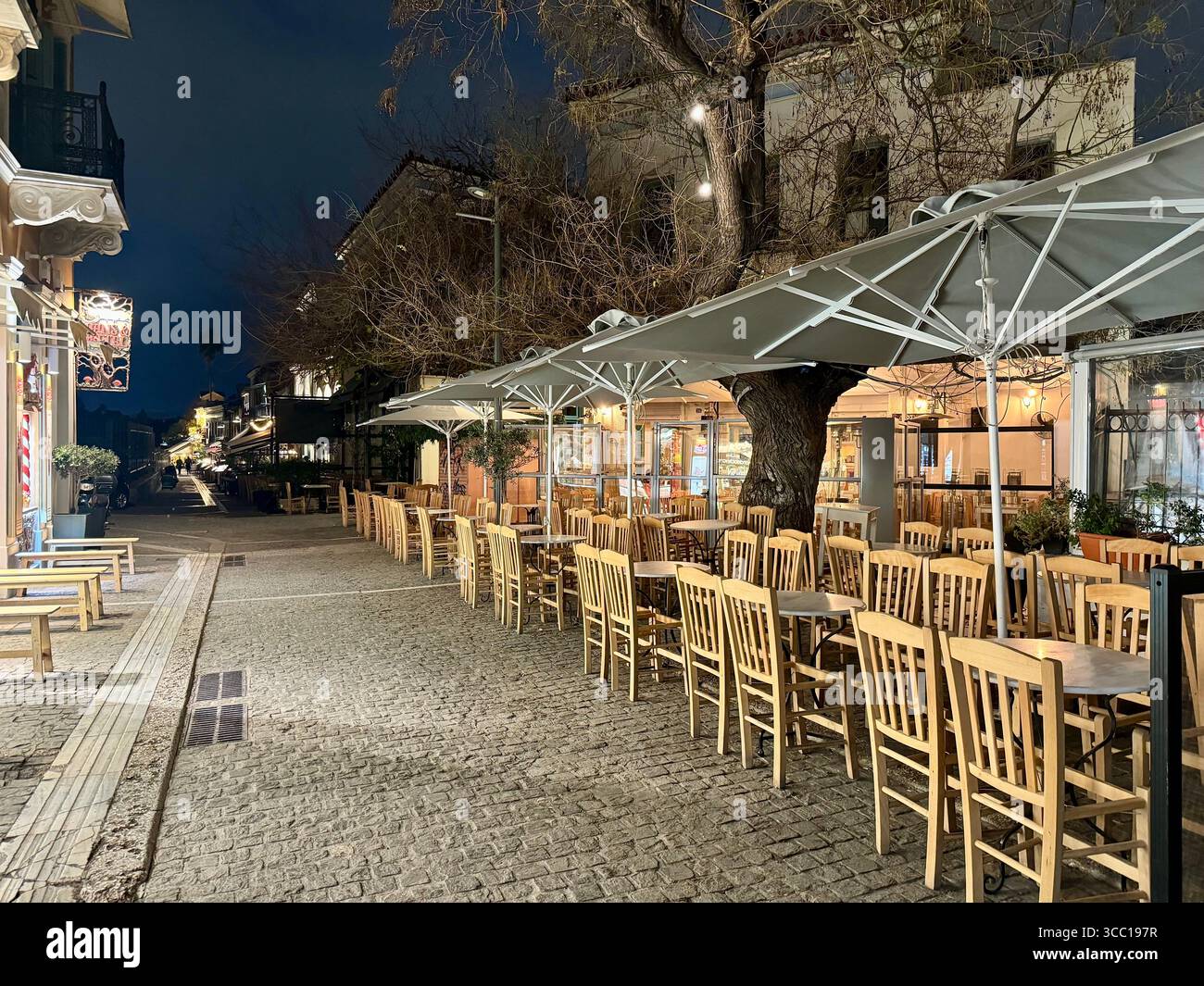 Leeres Café unter großen Sonnenschirmen in einer ruhigen Kopfsteinpflasterstraße in Athen, Griechenland. Stockfoto