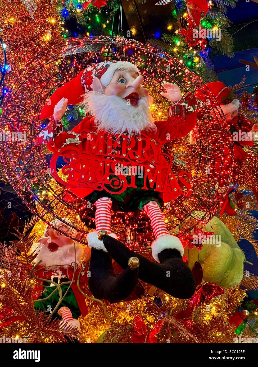Farbenfrohe Weihnachts-Elfendekoration umgeben von festlichen Lichtern und Ornamenten. - Smartphone-aufgenommenes Stockfoto