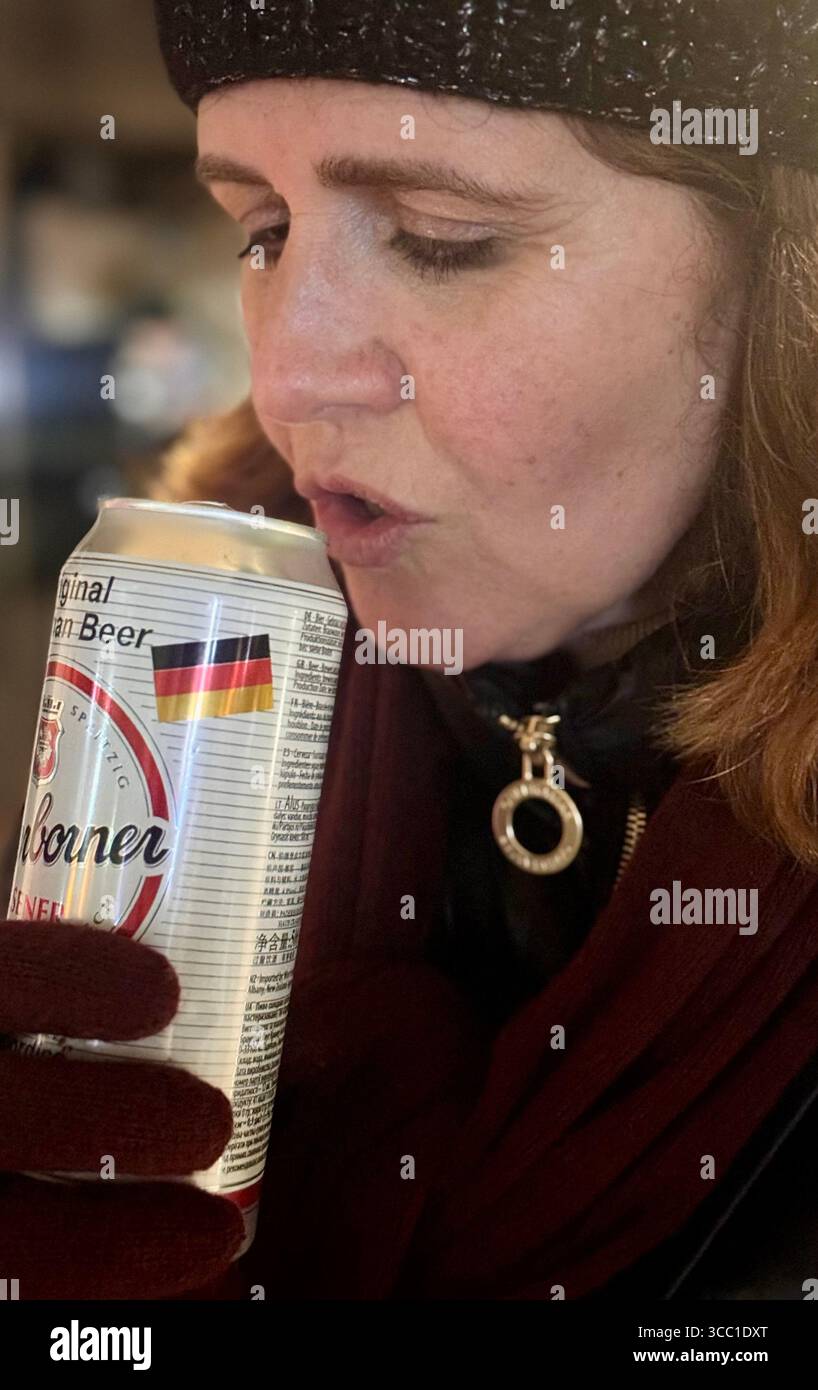 Frau, die im Winter gekleidet ist, schlürft draußen aus einer Dose bei kaltem Wetter. - Smartphone-aufgenommenes Stockfoto