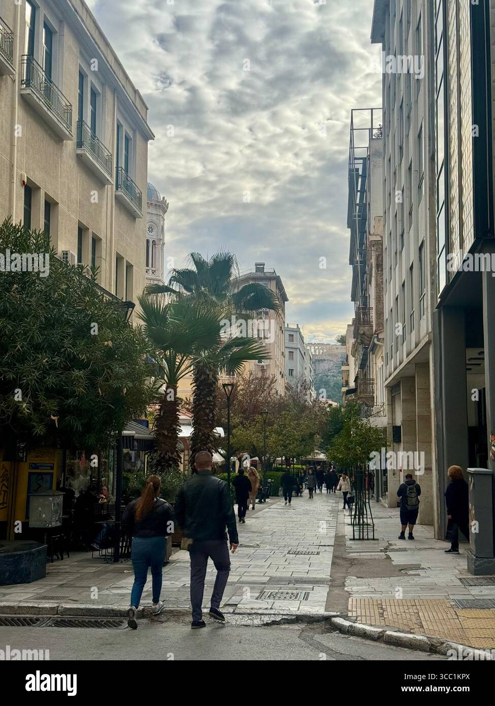 Die Straßenszene in der Innenstadt von Athen, in der Menschen unter einem bewölkten Himmel zwischen modernen Gebäuden spazieren gehen. - Smartphone-aufgenommenes Stockfoto