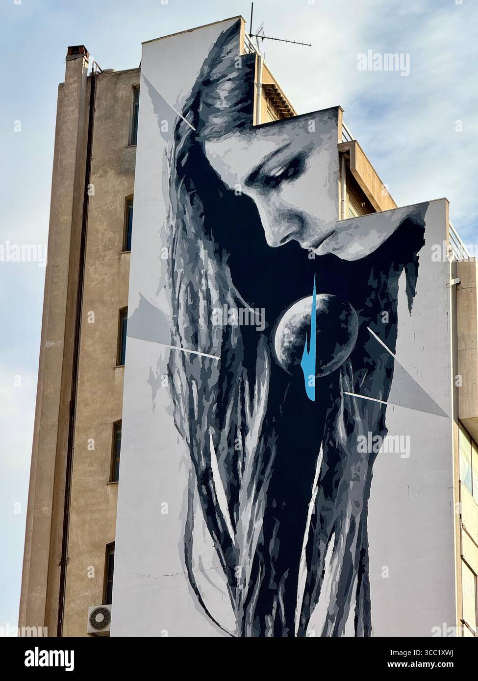 Großes Straßengemälde in einem Gebäude in Athen, das eine Frau mit langen Haaren und abstraktem Design zeigt. - Smartphone-aufgenommenes Stockfoto