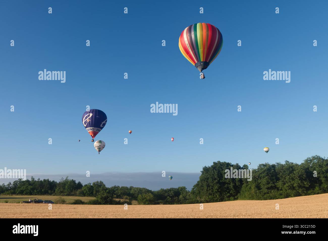 Eine Reihe von neun Heißluftballons, die über die französische Landschaft treiben Stockfoto