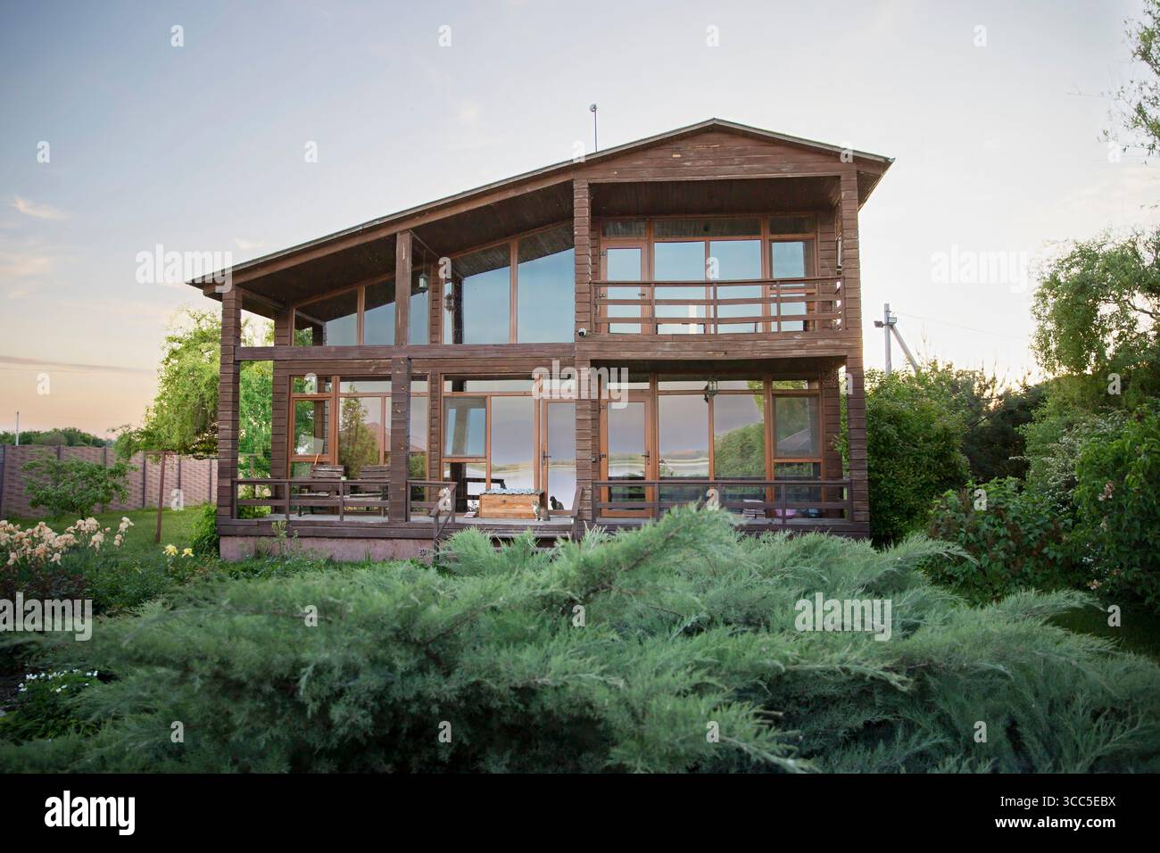 Hölzernes Landhaus mit großen Fenstern, umgeben von einem grünen Rasen und Bäumen, perfekt für Immobilien und Lifestyle Bilder Stockfoto