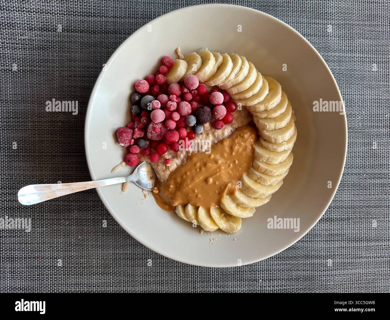 Hafer mit Bananenscheiben, gefrorenen Beeren und Erdnussbutter Stockfoto