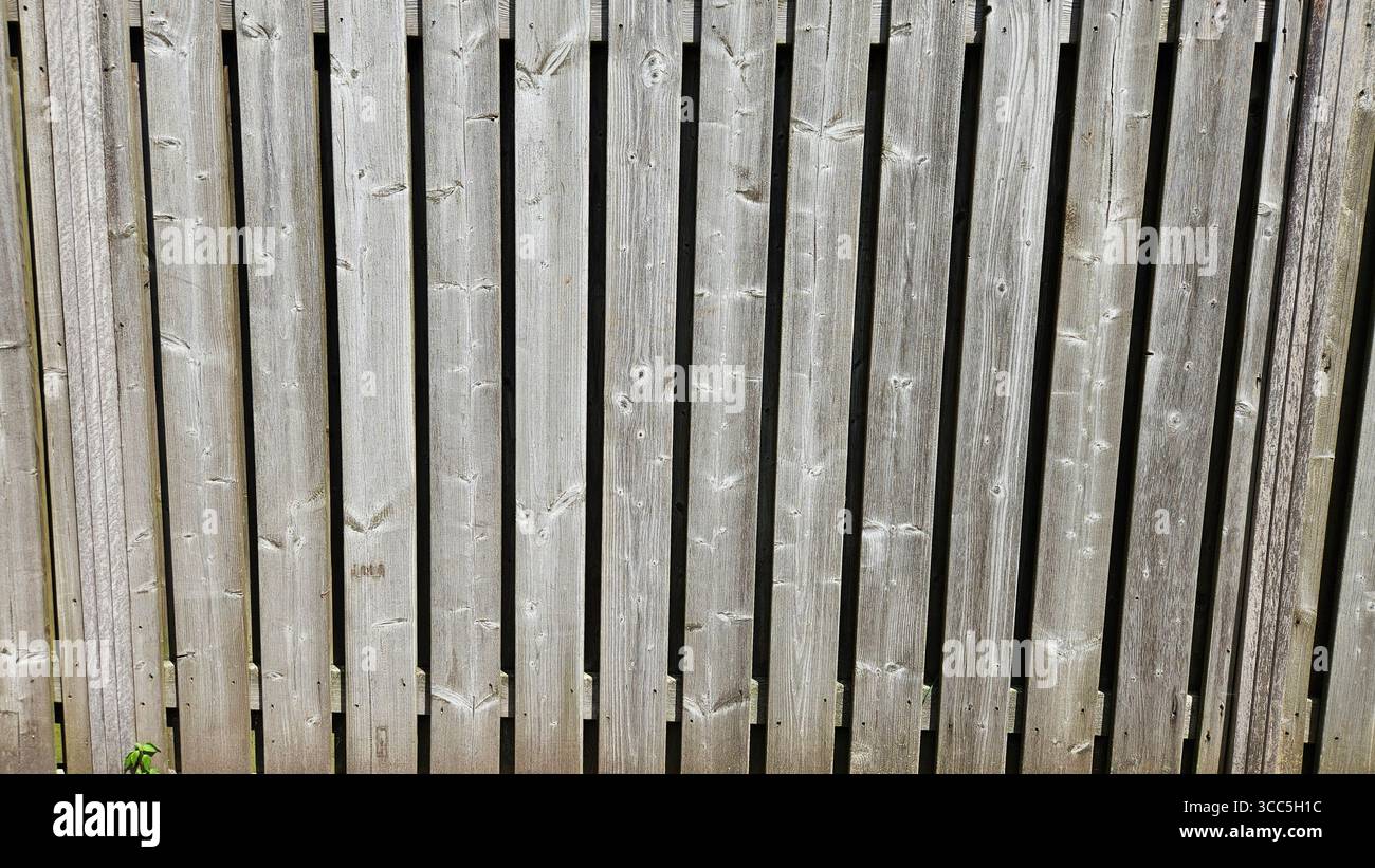 Nahaufnahme eines verwitterten Holzzauns mit vertikalen Dielen, die die rustikale Textur, Körnung und natürliche Alterung des Holzes hervorheben. - Smartphone-aufgenommenes Stockfoto