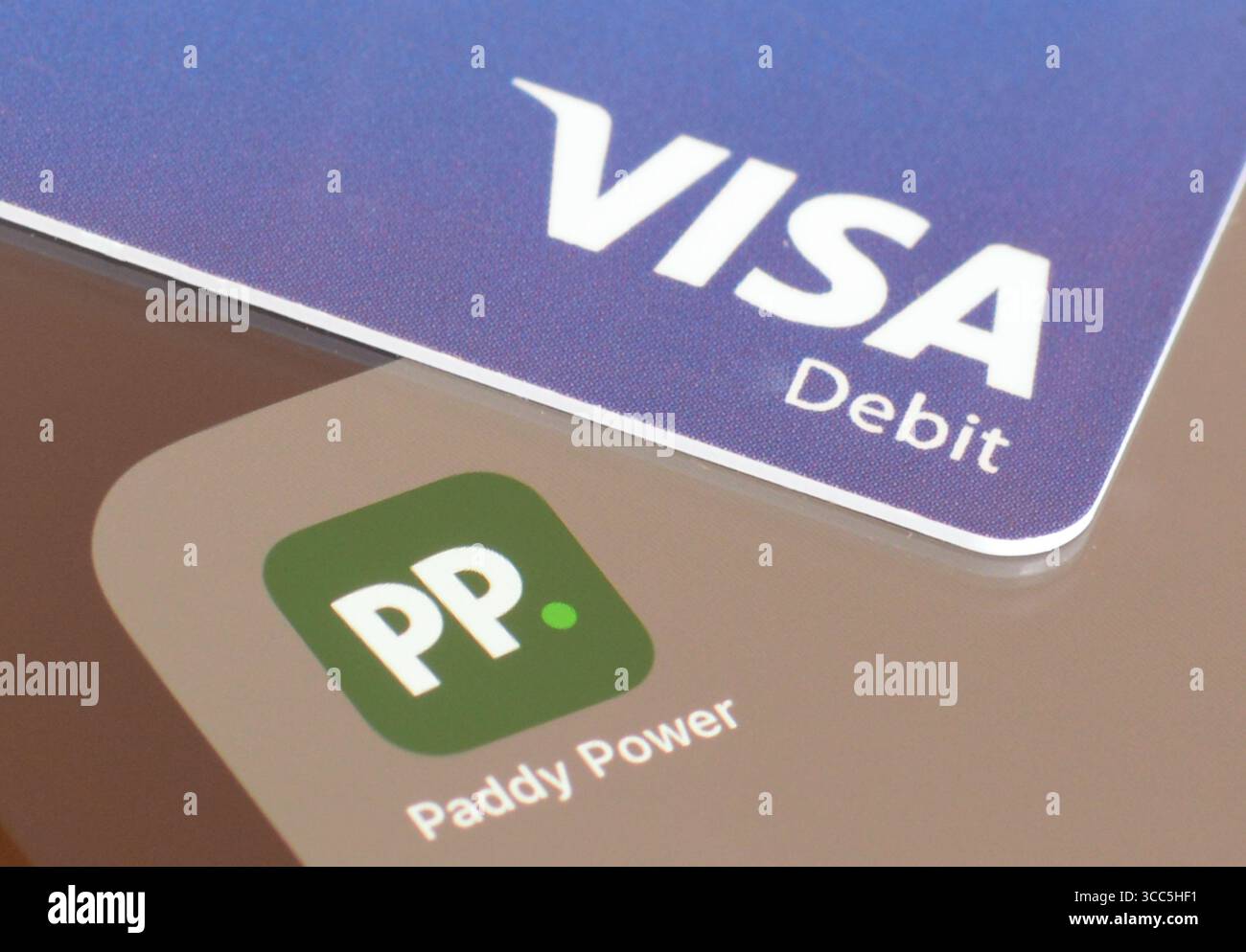 Paddy Power Glücksspiel-App auf dem Smartphone-Bildschirm mit VISA Debitkarte, um Geld einzuzahlen Stockfoto