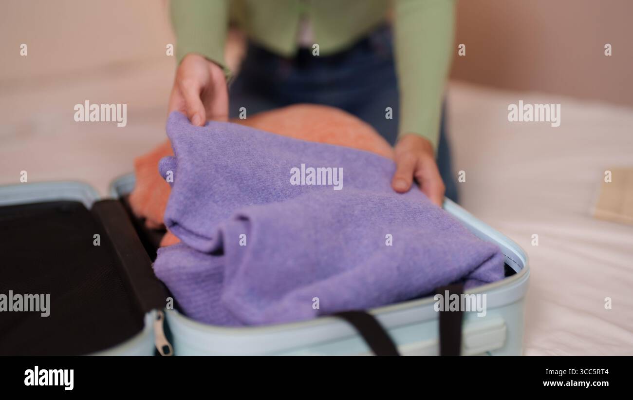 Die Hände für Erwachsene lassen sich ordentlich zusammenfalten und in einen offenen Reisekoffer auf einem Bett legen. Wichtige Vorbereitung auf eine anstehende Reise oder einen Urlaub. Stockfoto