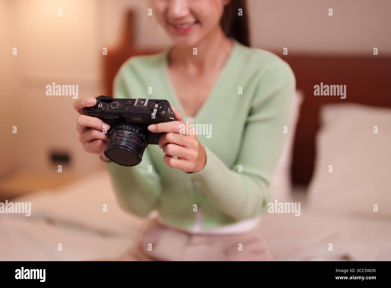 Asiatische Erwachsene Frau hält eine alte Kamera in einem gemütlichen Hotelzimmer. Festhalten von Reisemomenten, die sich auf eine aufregende Reise vorbereiten Stockfoto