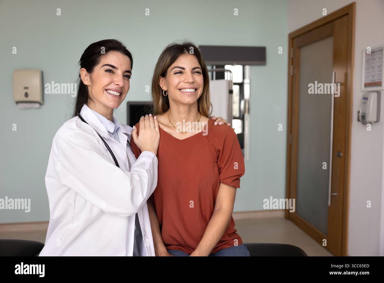Fröhlicher junger lateinischer Arzt, der die Schultern einer Patientin berührt Stockfoto